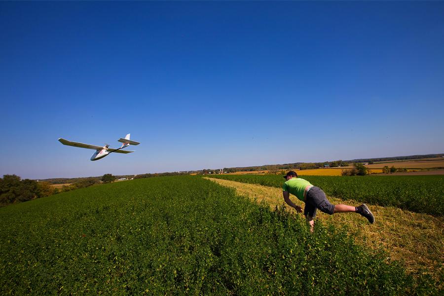 A student throws a GIS drone into the air in a field.