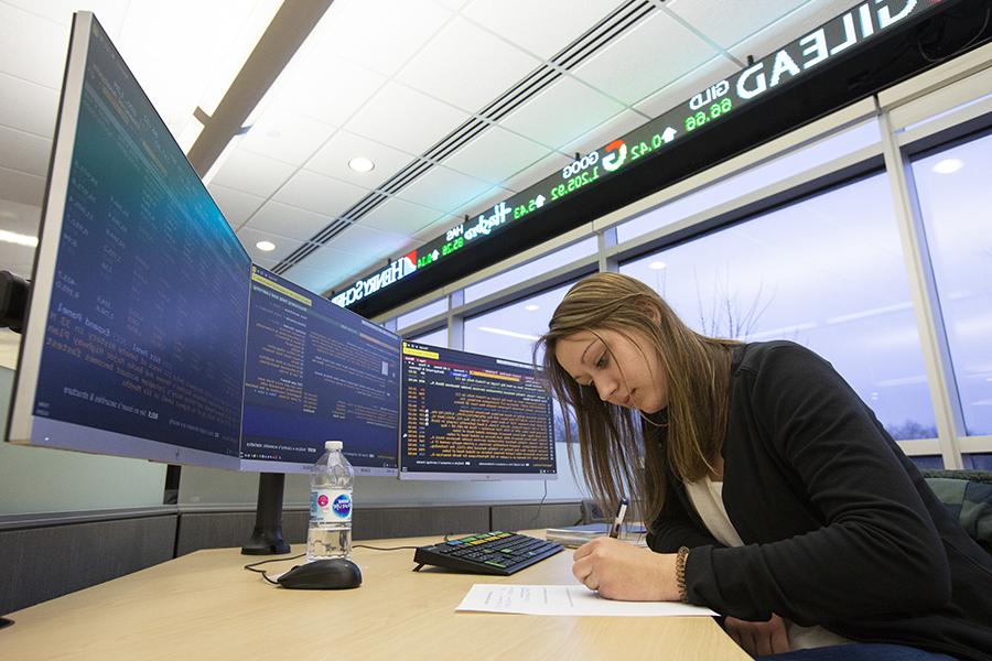 A student works at a desk in front of two computer monitors.