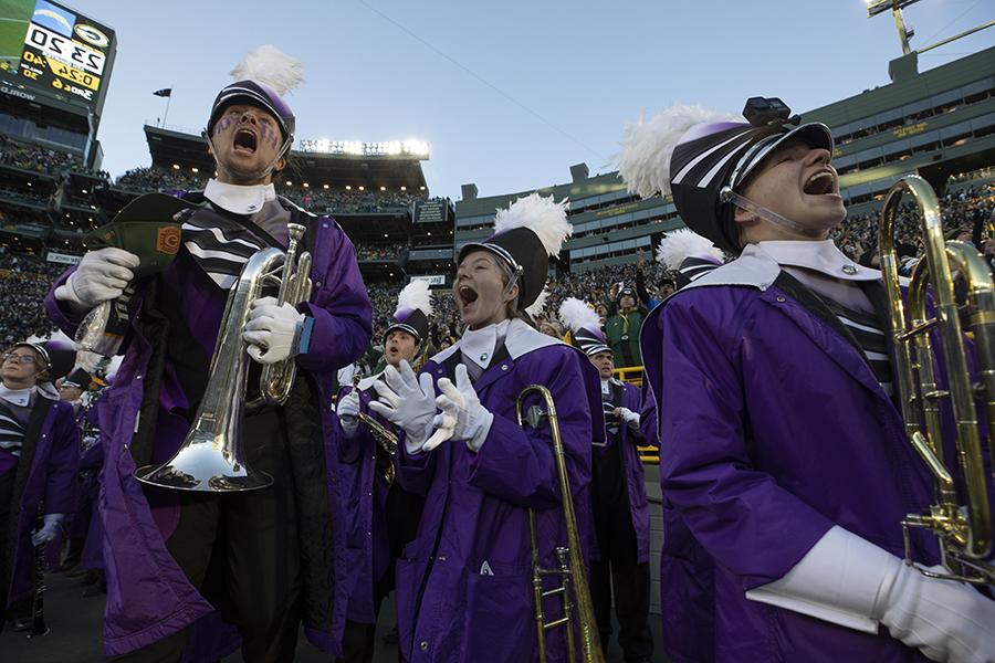 Students hold their instruments and yell with excitement while standing on the field at Lambeau Field.